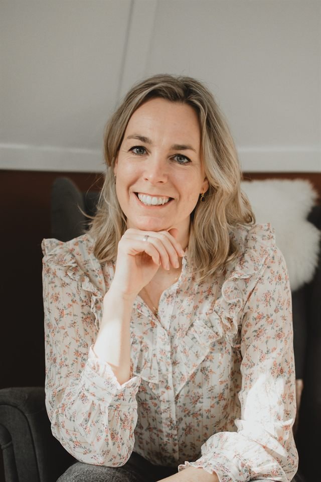 Yanieke Nijenkamp, lachend in een fauteuil met haar hand onder haar kin.